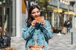© Andrei - cheerful young woman enjoying tasty waffles in front of a cafe in the street. take away food in the city