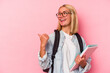 © Asier - Young venezuelan student woman isolated on pink background points with thumb finger away, laughing and carefree.