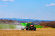 The tractor spreads granular fertilizer on a grass field. Agricultural work. Nitrate. Mineral fertilizers.
