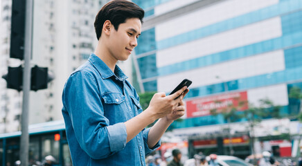 Young Asian man walking and using smartphone on the street