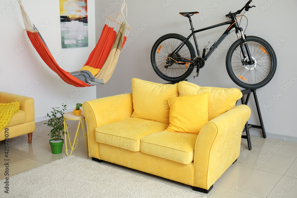 Stylish sofa with hammock and bicycle in interior of room
