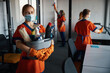 Female janitor with cleaning products standing among her busy colleagues