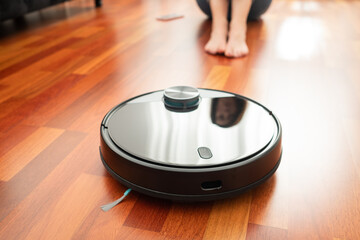 Wall Mural - Young girl feet when a round smart automatic vacuum cleaner passes to clean the floor, controlling machine housework robot