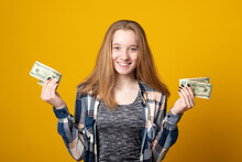 Happy Young Girl Holding Money Banknotes And Celebrating On Yellow Background. Girl Teenager Is Happy With The First Dollars Earned.