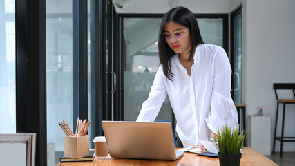 Young woman office worker standing and working on laptop computer at workplace.