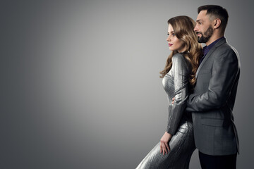 Wall Mural - Fashion Stylish Man Woman Profile Side View. Bearded Man in Suit holding Luxury Model. Elegant lady in Silver Dress with Boyfriend over Gray studio Background