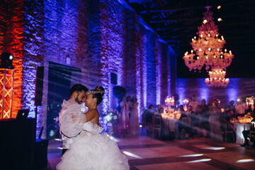 Wall Mural - The groom invites the bride to dance. Newlyweds are dancing in a large hall.