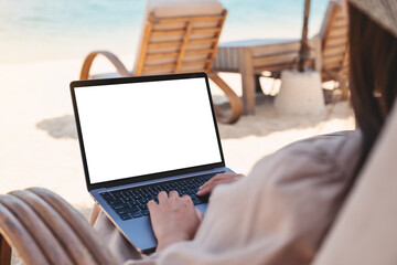 Mockup image of a woman using and typing on laptop computer with blank desktop screen while sitting on the beach