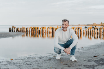 Wall Mural - Sporty trendy middle-aged man in jeans on a beach at sunset