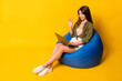 © deagreez - Photo of girl sit beanbag hold laptop wave hand screen wear green shirt skirt footwear isolated yellow color background