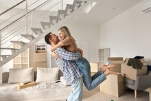 Happy Independent Couple First Time Home Owners Hugging In Living Room On Moving Day. Young Man And Woman Apartment Buyers Celebrating Relocation, Removal, Mortgage, New House Purchase Concept.
