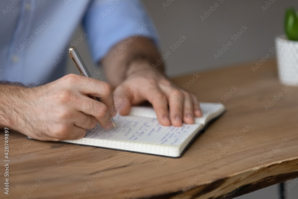 Crop close up of Caucasian man sit at desk write in notepad, make list or plan. Millennial male handwrite in notebook, involved in time management activity. Distant education, planner concept. - obrazy, fototapety, plakaty 
