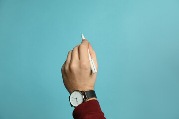 Left-handed man holding pen on light blue background, closeup