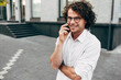 © iuricazac - Young employer man talking on a mobile phone with his colleague in the street. Handsome male with curly hair in a white shirt and eyeglasses making a call on his mobile phone in the city street.