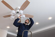 © New Africa - Electrician repairing ceiling fan with lamps indoors