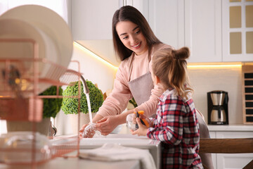 Mother and daughter washing dishes together in kitchen at home