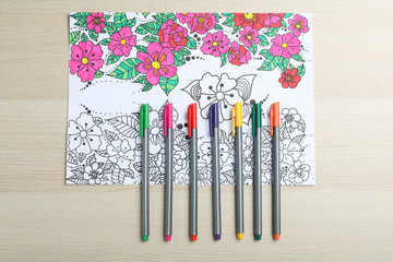 Poster - Antistress coloring page and felt tip pens on light wooden table, flat lay