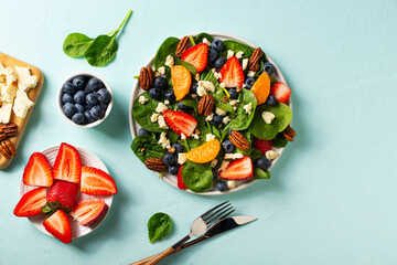 Summer salad with berries, cheese and spinach on blue background