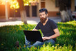 © endrews21 - Charismatic bearded male software developer with a long mustache in a shirt and jeans sits with a laptop on the green grass in the park. The guy talks to his parents by video link in nature