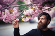 © endrews21 - Brutal bearded adult man with red beard and long mustache with gray hair near cherry blossom trees in spring