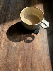 Empty cup of coffee with coffee stain and shadow cup of coffee shape on wooden table, Spot sun light from window, copy space