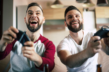 Excited Smiling Men Playing In Video Games On Tv At Home On The Couch. Friends With Joysticks Play Game With Happy Emotions On Faces