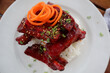 Closeup of spare ribs dish on a bed of rice with chives and shaved carrot garnish rosemary garnish