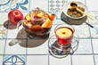 Fruit tea with apples and thyme in glass teapot and cup on table made of colored tiles