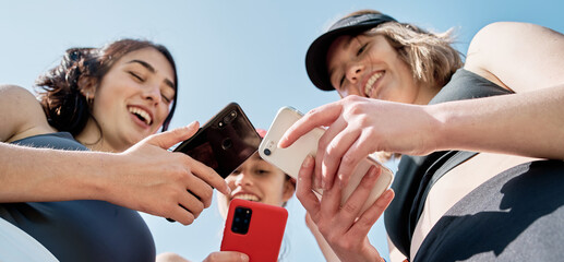 three beautiful young friends laughing while looking at their cell phones after practicing sports,view from below of three smiling girls with their cell phones.