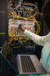 © Seventyfour - Vertical close up of female network engineer connecting cables in server cabinet while working with supercomputer in data center, copy space