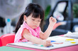 © Kanthita - Girl is using chalk paint on her creations. Child makes art on white drawing paper that is pinned on plywood board. Building imagination for children. A 4 year old kid making crafts. Study from home.