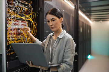 Waist up portrait of female network engineer connecting cables in server cabinet while working with supercomputer in data center, copy space