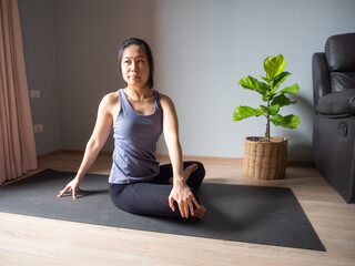 Wall Mural - seated spinal twist pose yoga asian woman home workout fitness body weight exercise pilates health training sport healthy lifestyle activity wellness care on mat indoors natural light selective focus