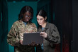 © Seventyfour - Waist up portrait of two young women wearing military uniform using laptop while standing in server room, copy space
