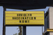 © Ole - Billboard saying Covid-19 Vaccination Now! With palm trees and blue sky background. Coronavirus pandemic vaccine concept.