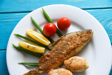 Fried fish on a plate with vegetables, lemon and onion