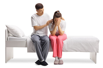 Wall Mural - Young female in pajamas sitting on a bed crying and a guy comforting her