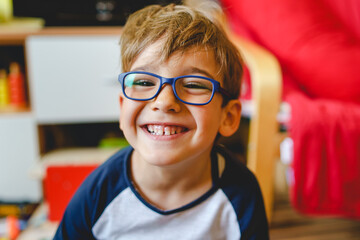 portrait of happy caucasian boy with eyeglasses sitting at home in room in day real people small mal
