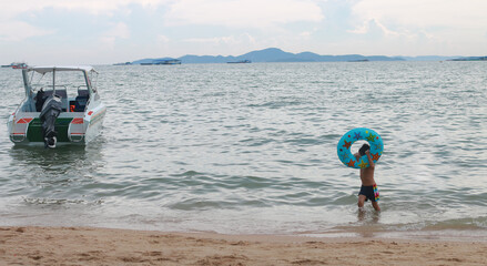 Wall Mural - The boy was holding a swim ring playing in the sea with a speedboat parked nearby