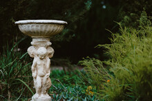 Beautiful Ceramic Garden Bird Bath Ceramic Statue Decorated With Small Children Surrounded By Lush Foliage