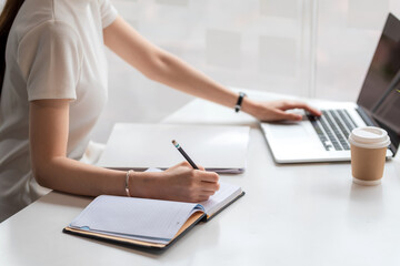 Close up of woman taking notes and using laptop at the home.