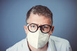 portrait of man with gray hair and blue shirt with mouth nose mask and black glasses during Corona pandemic in front of blue background