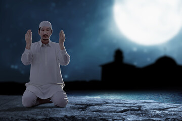 Wall Mural - Asian Muslim man sitting while raised hands and praying