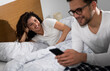 © Zoran Zeremski - Man using phone in bed while woman looking at him.