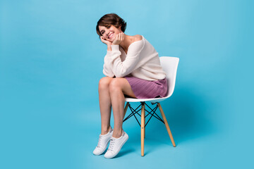 Poster - Photo portrait full body view of cute girl with head on hands sitting on chair isolated on pastel blue colored background