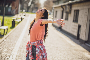 Happy young woman is enjoying sunny day outdoor in city.