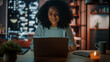 © Gorodenkoff - Beautiful Authentic Latina Female Sitting at a Desk in a Cozy Dark Living Room in the Evening and Using Laptop Computer at Home. She's Browsing the Internet and Checking Videos on Social Networks.