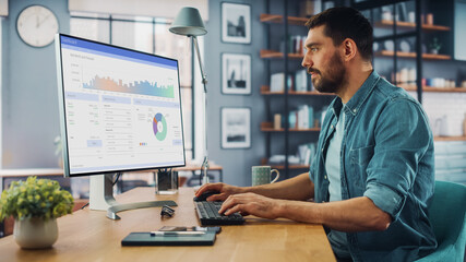 Caucasian Specialist Working on Desktop Computer in Creative Home Living Room. Freelance Male is Doing Market Analysis and Creates Report with Charts for Clients and Employer.