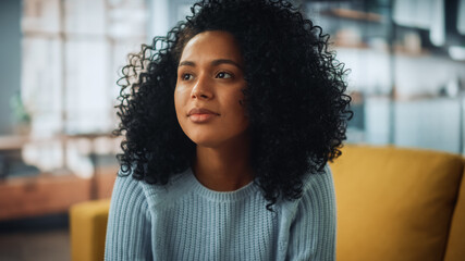 Portrait of a Beautiful Authentic Latina Female with Afro Hair Wearing Light Blue Jumper and Glasses. She Looks Away and Thinking about Life. Successful Woman Resting in Bright Living Room.