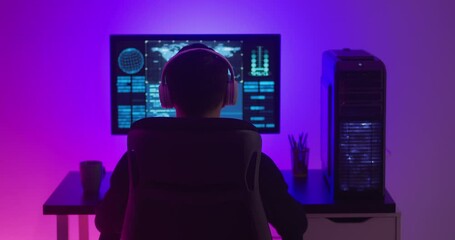 Man programmer in headphones working at a computer in data center at night. Dangerous hacker working in cyber security center filled with neon light.